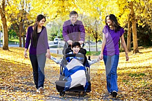 Family with disabled child in wheelchair walking among autumn le