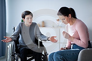 Family disagreement. Upset mother crying and her teenage son in wheelchair trying to justify himself at home photo