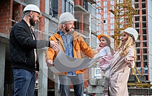 Family discussing building plan with architect at construction site.