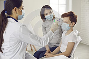 Family doctor measuring little boy`s temperature with non-contact digital thermometer