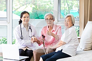 Family doctor or nurse wearing white coat and stethoscope with smiling senior patient during home visit,young female home caregive photo