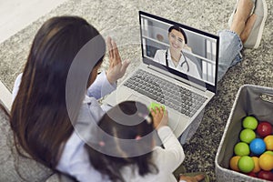 Family doctor online. Mother and baby greet the doctor have a video call laptop to the doctor at home.