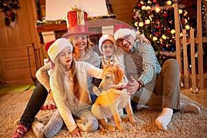 Family and dog sitting by Christmas tree
