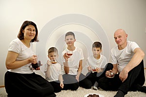 family drinks tea sitting on the floor on a white carpet in front of them cookies mom holds jug