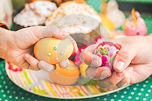 Family Easter tradition. Daughter and mother beating Easter eggs against Kulich or easter cake