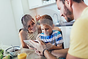 Family eating breakfast at kitchen table and using digital tablet