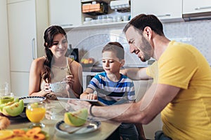 Family eating breakfast at kitchen table and using digital tablet