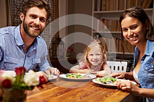 Family eating dinner at a dining table, looking at camera