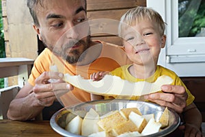 Family eating fresh sweet melon on terrace. Father and his toddler son biting together slice of honeymelon fruit. Summer healthy