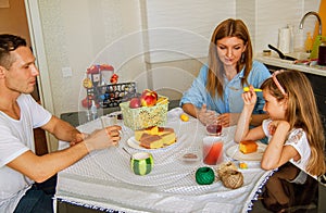Family, eating and people concept - happy mother, father and daughter having breakfast at home.
