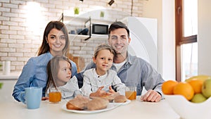 Family, eating and people concept - happy mother, father,daughter and son having breakfast at home on modern kitchen