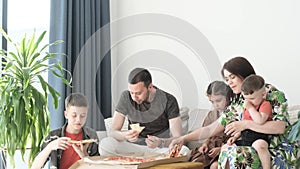 Family eating pizza sitting on sofa at home. Husband and wife with children eating delicious pizza