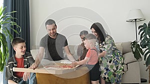 Family eating pizza sitting on sofa at home. Husband and wife with children eating delicious pizza