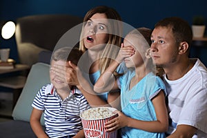 Family eating popcorn while watching scary movie in evening