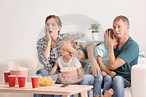 Family eating popcorn while watching scary movie at home