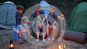 Family enjoying camping in forest, mother and two children sitting around on straw bale beside balefire, mom and kids