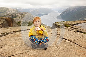 Family, enjoying the hike to Preikestolen, the Pulpit Rock in Lysebotn, Norway on a rainy day, toddler climbing with his pet dog