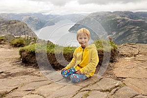 Family, enjoying the hike to Preikestolen, the Pulpit Rock in Lysebotn, Norway on a rainy day, toddler climbing with his pet dog