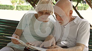 Family enjoying vacation. Seniors sitting on bench in park studying city map looking for showplaces