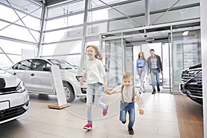 Family entering car dealership, happy children running.