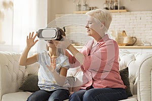 Family entertainments. Cute child in VR headset playing video games and her grandmother at home