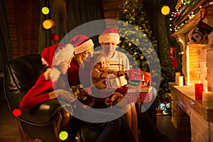 Family exchanging gifts in front of fireplace at Christmas tree