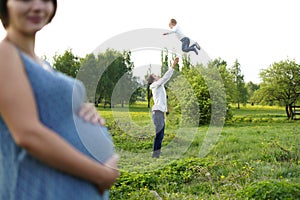 Family. Family Portrait. Young happy Family walking outdoor. Pregnant woman, husband and Child. Dad throws his son up in