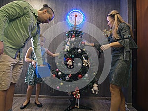 The family fast and fanny decorates the Christmas tree. Side view. Time on the clock is 23.45 on wall.