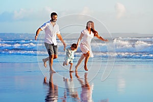 Family - father, mother, baby run on sunset beach