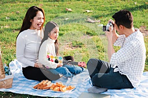 Family father, mother and child having fun and enjoying outdoor together sitting on the grass party with shooting photos