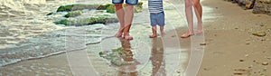 Family Father mother and little son walk barefoot along the seashore on the wet sand