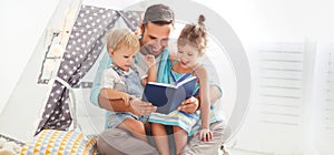 Family father reading to children book in tent at home