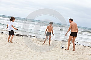 Family father two kids playing football on beach