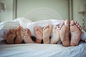 Family feet sticking out from under the bed sheet