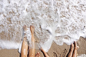 Family feet wet by the sea waves at the beach in summer holiday