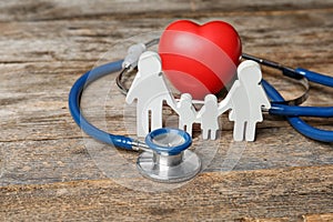 Family figure with stethoscope and heart on wooden background.