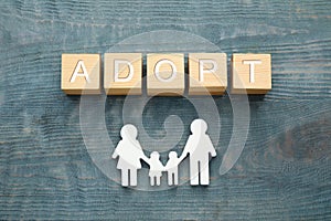 Family figure and word Adopt made of cubes on blue wooden table, flat lay