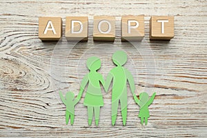 Family figure and word Adopt made of cubes on white wooden table, flat lay