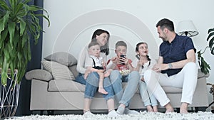 A family of five - father, mother and daughter and sons are watching TV in the evening.