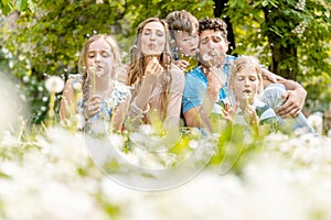 Family of five sitting on a meadow blowing dandelion flowers