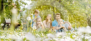 Family of five sitting on a meadow blowing dandelion flowers