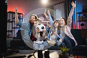 Family football fans sitting on sofa at home in the evening and celebrating winning and scored goal