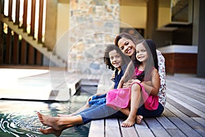 Family is forever. a mother with her two children dipping their feet into the pool on the patio.