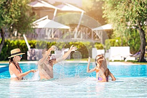 Happy family of four in outdoors swimming pool