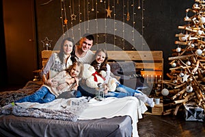 A family of four hugging in front of the christmas tree on the bed. New year`s eve. happiness and big family concept