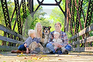 Family of Four People and Dog Sitting On Bridge in Autumn