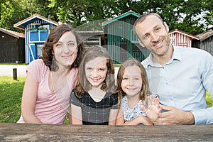 Family of four sit on wood table on park in summer spring day