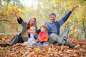 Family of four sits in autumn park.