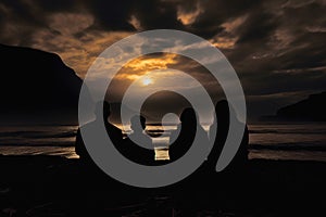 Family of four sitting on ocean shore and looking at dramatic orange sunset at dusk, rear view