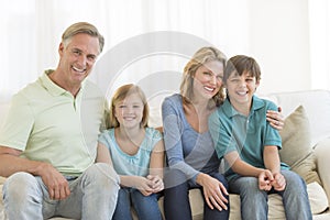 Family Of Four Smiling Together On Sofa